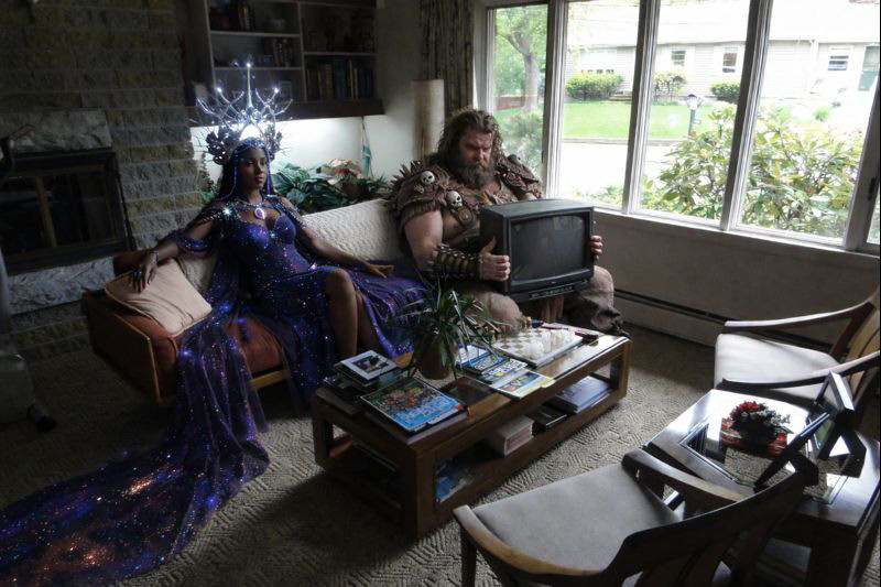 Крупный план фото с Галактической королевой, варваром и добавленным на диван ЭЛТ-монитором, созданный GPT Image 1.5